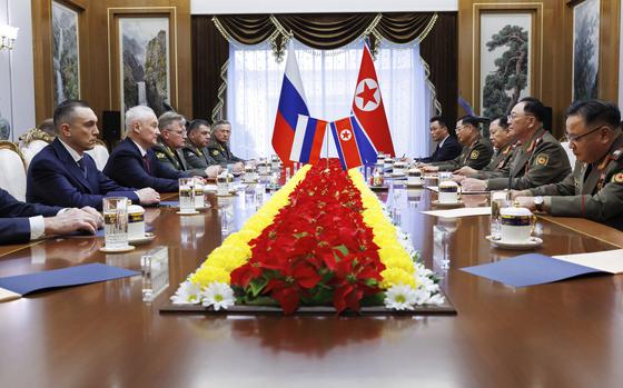 Russian and North Korean officials sit across from each other on opposite sides of a long table with the countries’ flags in the background.