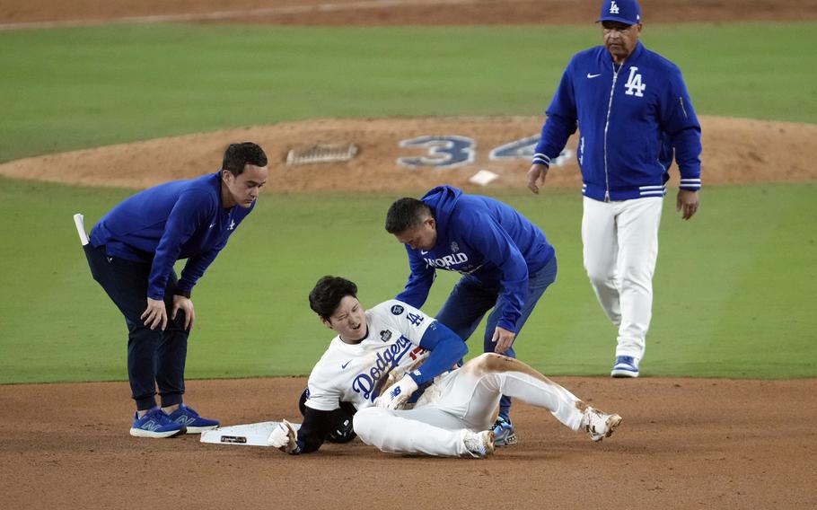 A baseball player lays on the ground of the baseball diamond and grimaces in pain.