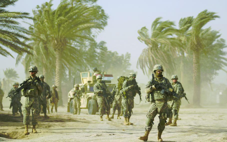 Soldiers from 1st Platoon, Company A, Task Force 3-66 Armor and Iraqi troops wait in gusting winds before heading out on patrol Feb. 20, 2009 in the village of Tahweela, Iraq. Operation Dark Wolf Pursuit One aims to execute the "clear, hold and build" strategy in the southern Balad-Ruz District of Iraq's Diyala province.