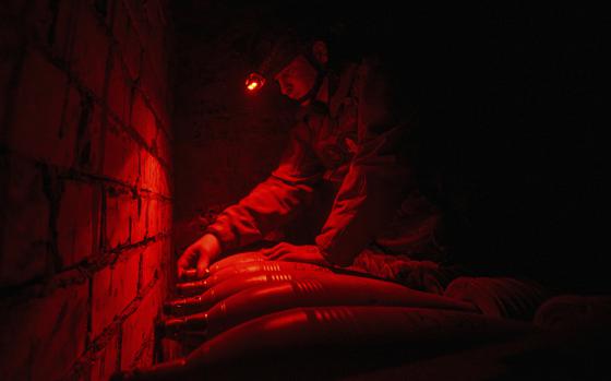 A Ukrainian serviceman kneels down to prepare a mortar in the glow of a red light.