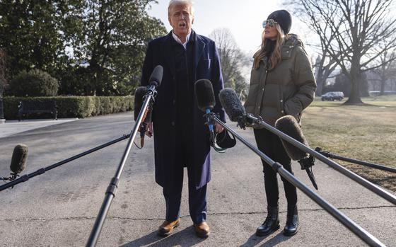 President Trump is seen from head to toe with several microphones in front of him and first lady Melania Trump to his side.