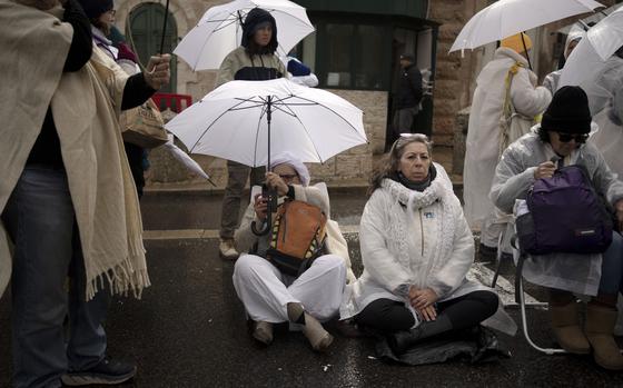 Two women wearing white sit on the street as a demonstration.