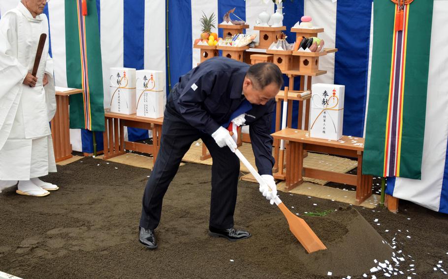 A man uses a ceremonial wooden tool to break ground on a construction project.