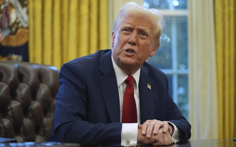 President Trump tilts his head up and speaks while seated with his hands folded on the desk.