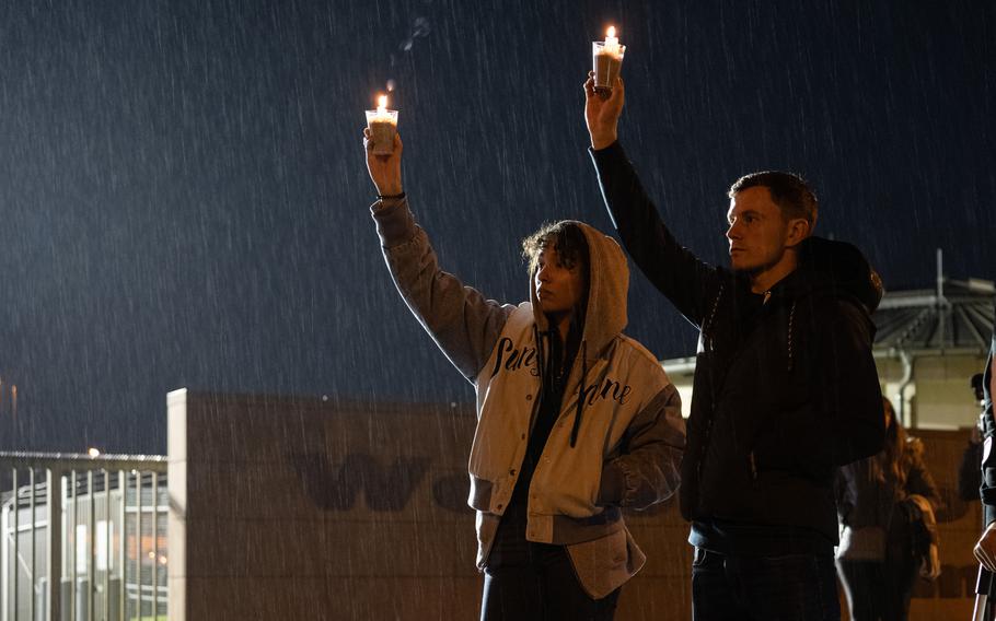 A man and a woman hold up cups with candles inside as rain pours down during a protest at the main gate at Spangdahlem Air Base.