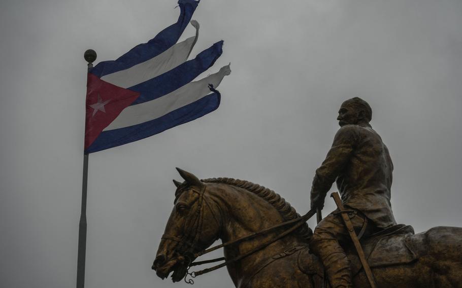 A windtorn Cuban flag flies above a statue of a man on horeseback.