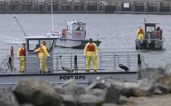 Small boats with personnel in yellow suits and orange life jackets, seen from the shore.