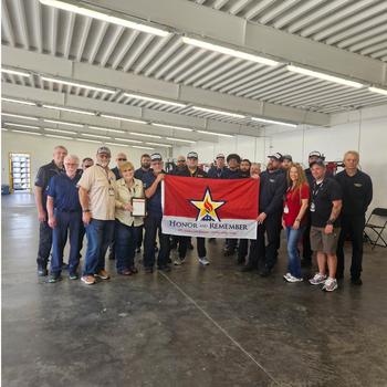 A group of people hold up a flag that says “Honor and Remember” for a photo