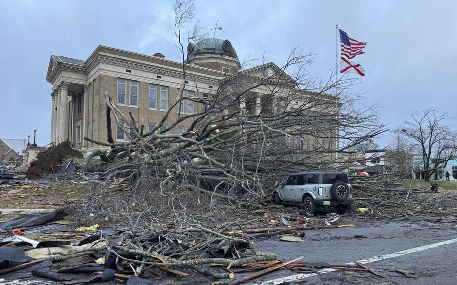 Trees are down and branches are scattered in front of a building.