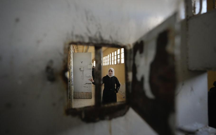 A woman wearing a hijab is seen through a small window of a prison cell door.