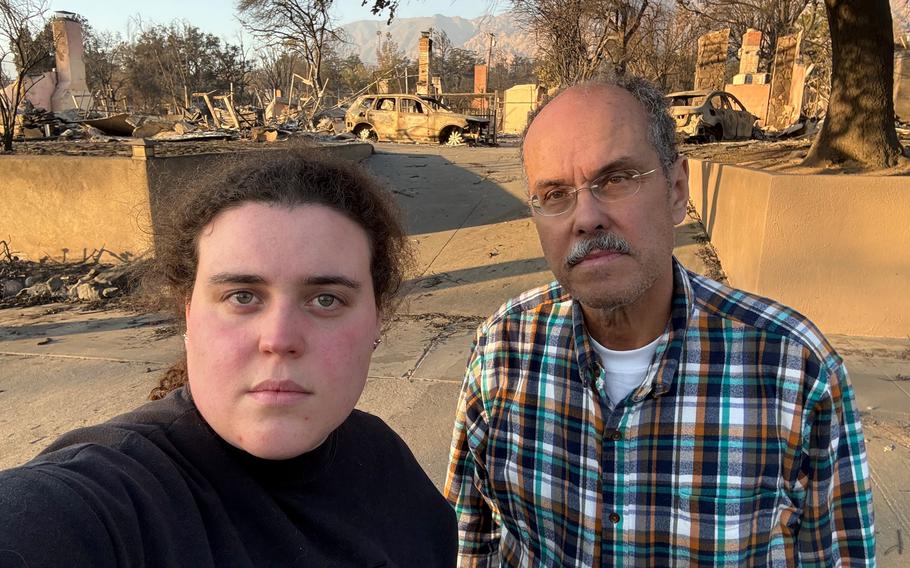 Two people pose for a photo. Behind them is damage from the Eaton fire.