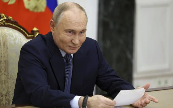 Vladimir Putin holds a stack of documents while seated at a desk.