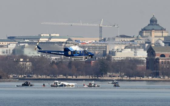 A U.S. Park Police helicopter flies over boats in a river with a city skyline in the background.