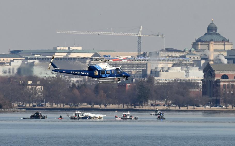 A U.S. Park Police helicopter flies over boats in a river with a city skyline in the background.