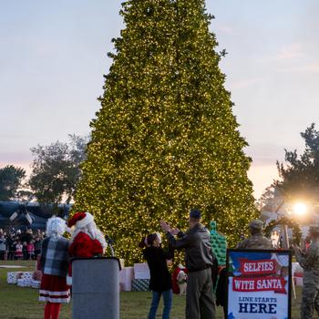 The tree is lit at Hurlburt Field. A sign in front announces Selfies with Santa.