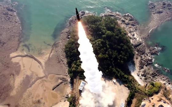 A ballistic missile, seen from above, rises into the sky from a coastal launch site.