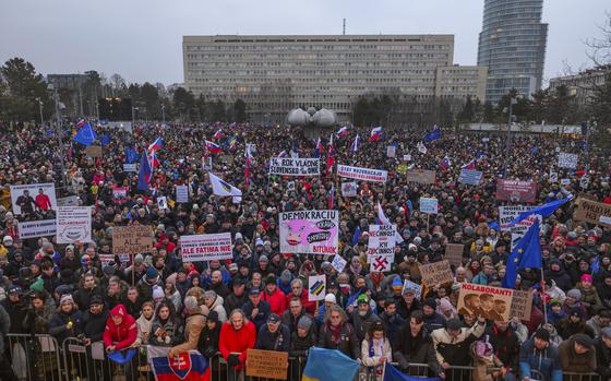 A mass of people, many of them holding large signs or flags, in a square encircled by buildings.