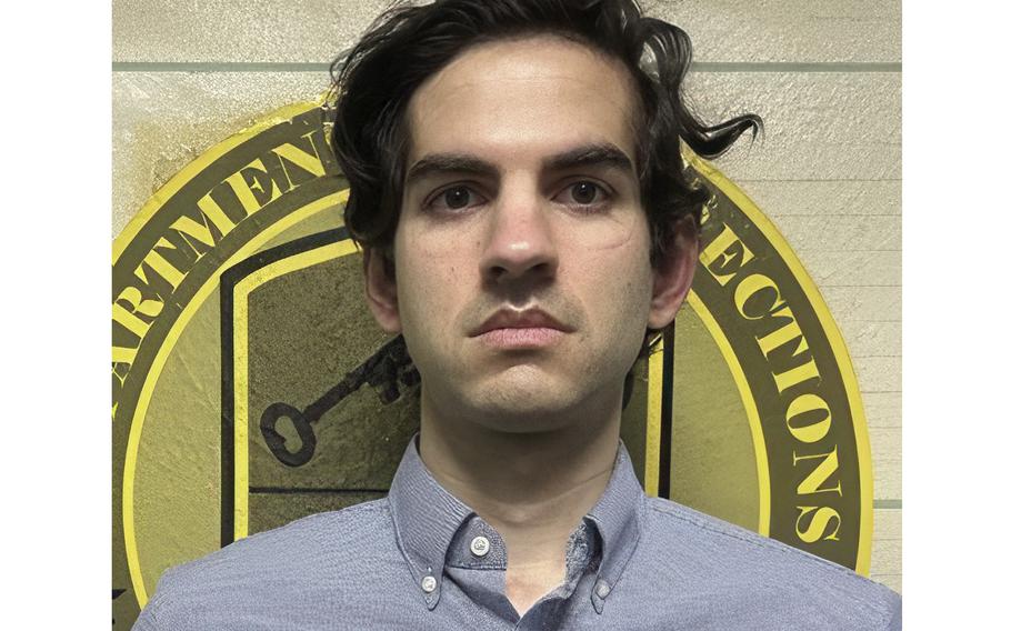 An unsmiling man with apparent mask lines on his forehead and around his eyes stands in front of a yellow department of corrections seal.