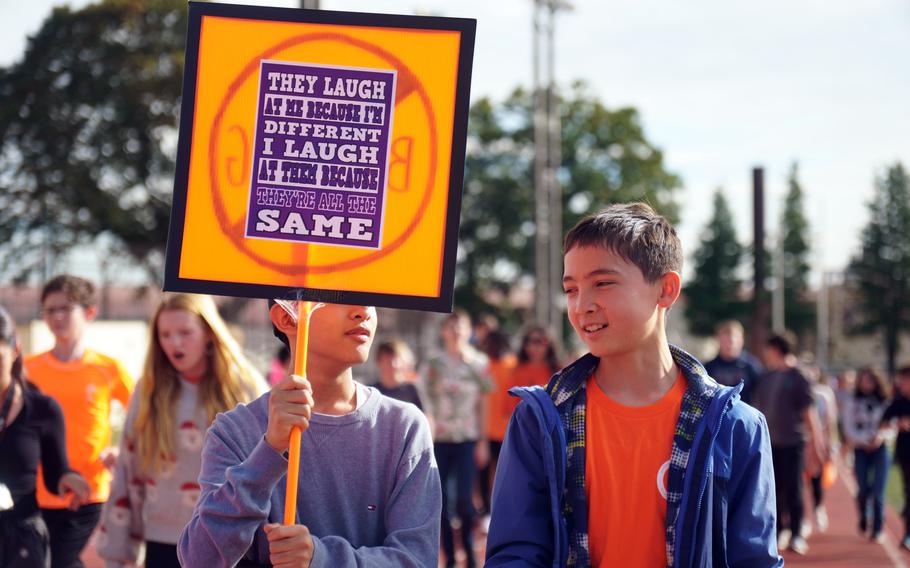 A student walking on a track holds a sign that reads: 'They laugh at me because I'm different. I laugh at them because they are all the same.”