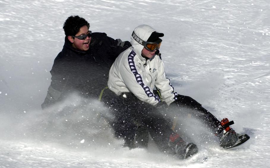 Two people on a sled kick up snow as they skid to a stop.