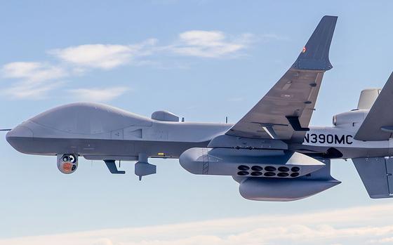 A large military drone flies above clouds.