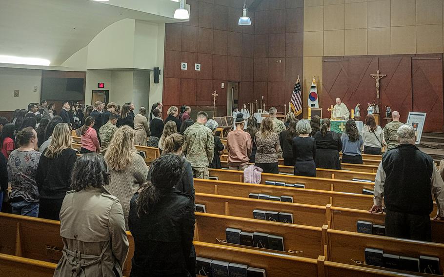 Mourners stand in front of church pews with their heads bowed during a memorial service.