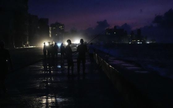 People stand in a group in the darkness of a blackout illuminated from behind by car headlights.