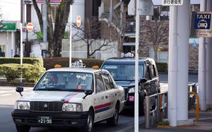 Two taxis parked in front of sign that reads, “taxi” and “taxi stop” in both English and Japanese.