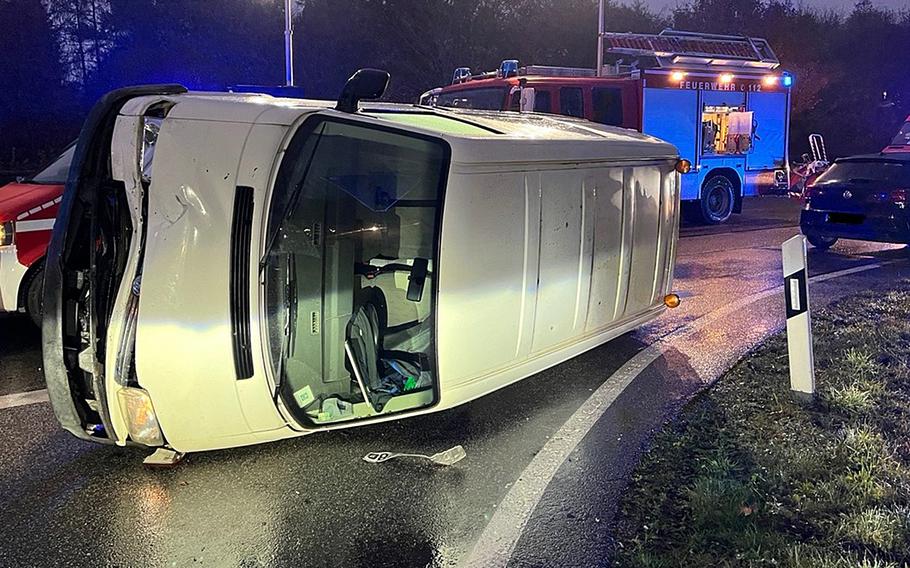 A white car sits on its side on a road with a firetruck in the background.