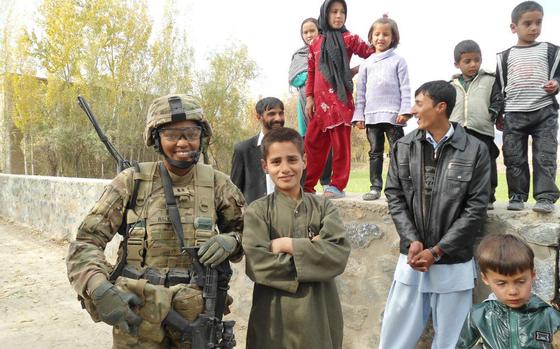 A woman in combat gear stands next to an Afghan boy.