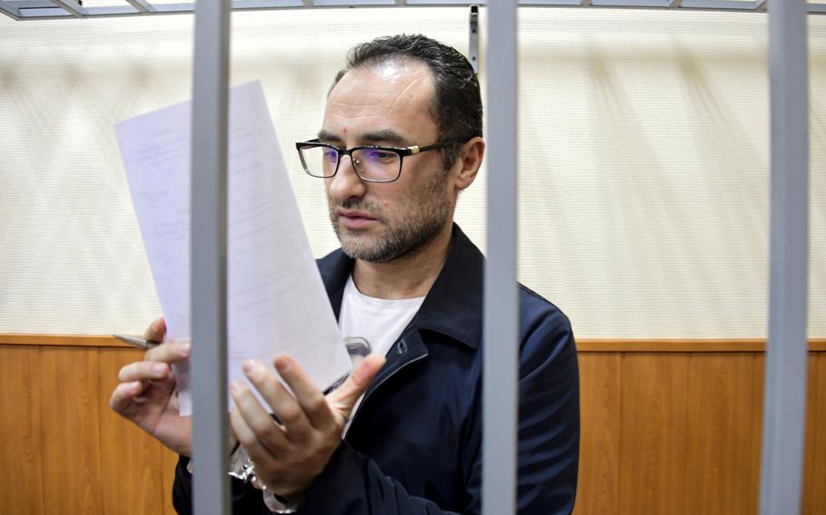 A man holds a piece of paper with handcuffed hands and bars in front of him.