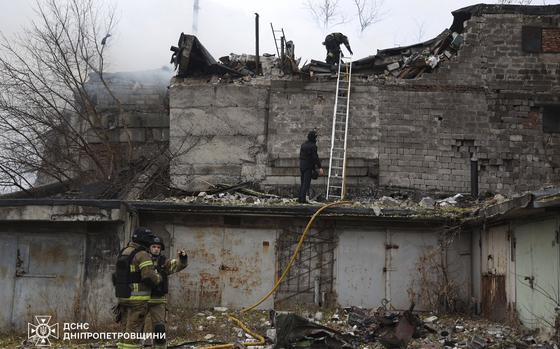 Firefighters and rescue worker stand next to and on a damaged building.