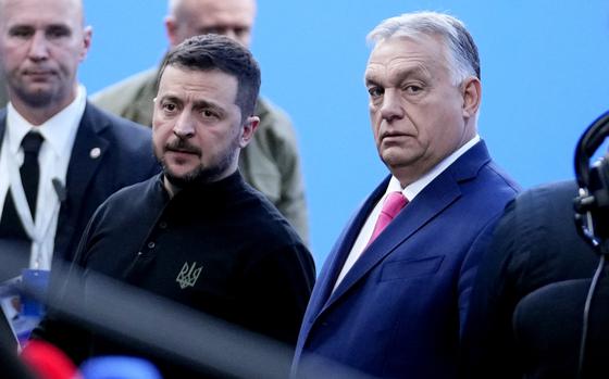 Ukrainian President Volodymyr Zelenskyy stands next to Hungarian Prime Minister Viktor Orban while photographers take pictures.