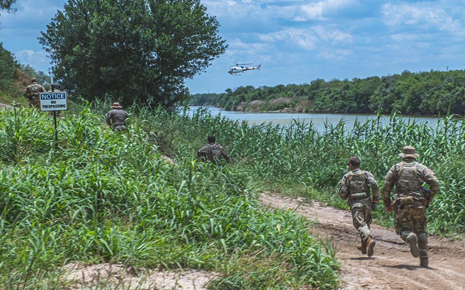 Members of the Texas National Guard watch a Border Patrol helicopter hover above a group of civilians wading in the Rio Grande River along the Texas-Mexico border, on May 22, 2023. 