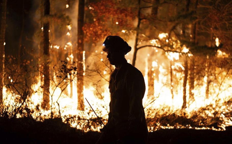 A firefighter is silhouetted against a forest fire