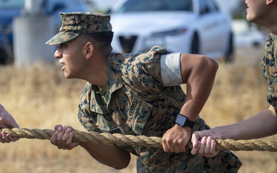 A Marine wearing a blouse with sleeves up tugs on a rope.