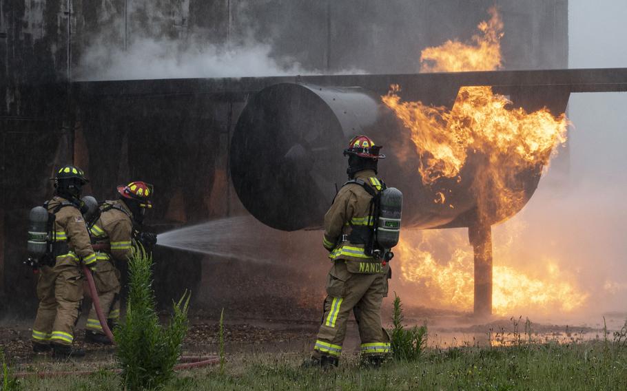 Firefighters in heavy suits and helmets spray water on a burning airplane engine during an exercise.