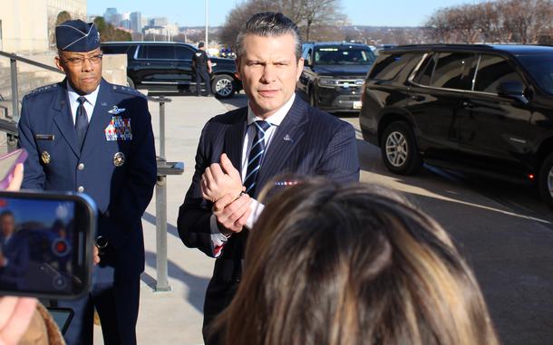 A man in a dark suit speaks to reporters on the steps of the Pentagon while standing next to a military officer in dress uniform.