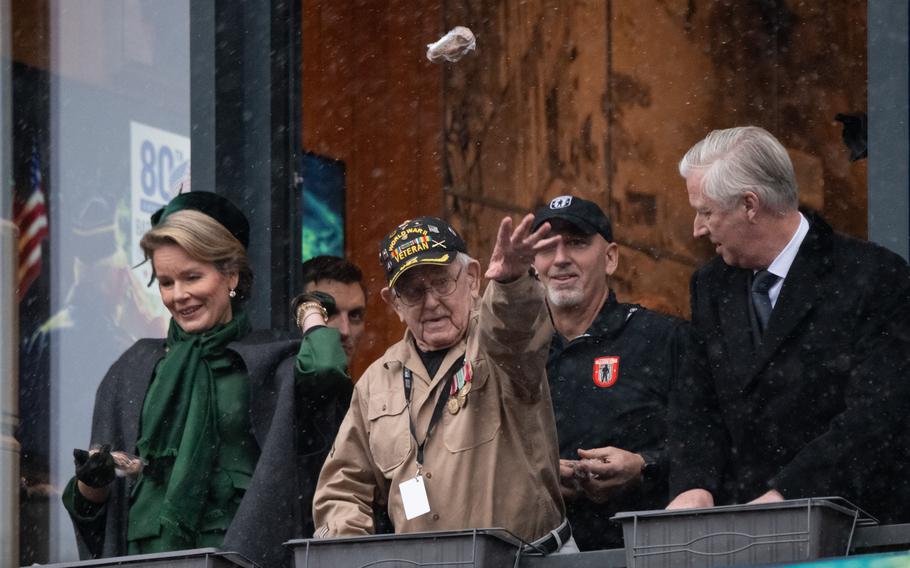 An American WWII veteran in the center of the photo throws nuts from a balcony, with two people at either side of him.