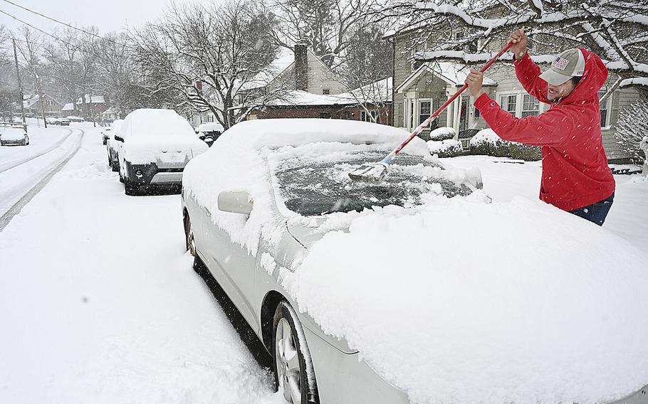 A man sweeps snow off his car in front of his house.