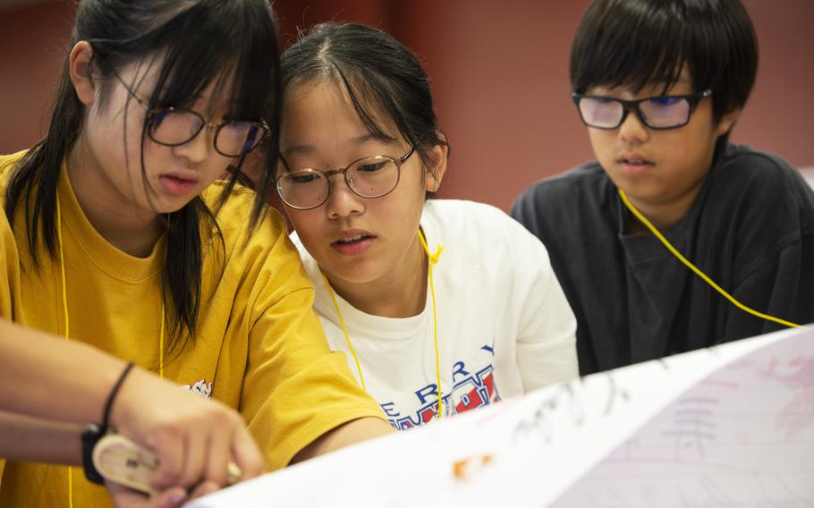 Japanese students Naji Takemoto, 15, left, Wakana Terasaki, 15, middle, and Mitsuki Kawamoto, 13, right, design a poster during the Student Educational Exchange and Dialogue at Matthew C. Perry High School, Marine Corps Air Station Iwakuni, Japan, Sept. 8, 2024.