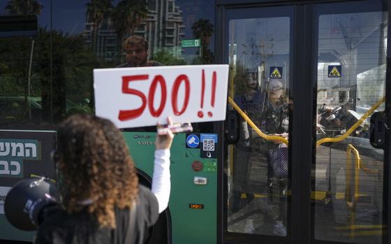 A protester next to a bus holds a bullhorn and a sign that says 500!!