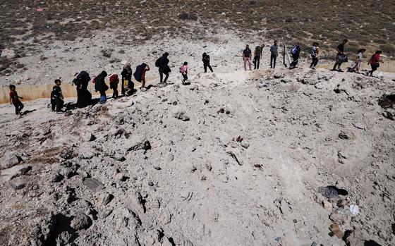 People carry their luggage as they cross into Syria on foot, through a crater caused by Israeli airstrikes aiming to block Beirut-Damascus highway at the Masnaa crossing, in the eastern Bekaa Valley, Lebanon, Saturday, Oct. 5, 2024. (AP Photo/Hassan Ammar)