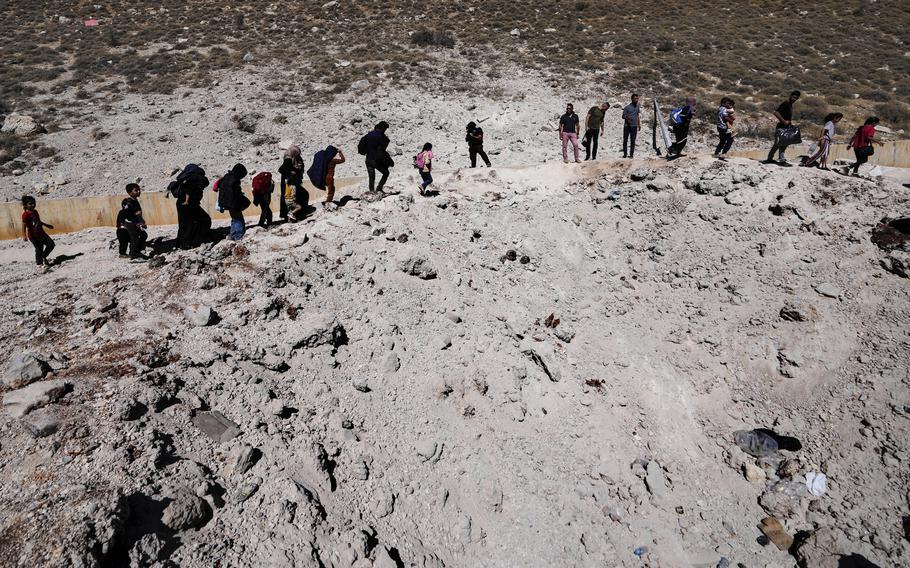 People carry their luggage as they cross into Syria on foot, through a crater caused by Israeli airstrikes aiming to block Beirut-Damascus highway at the Masnaa crossing, in the eastern Bekaa Valley, Lebanon.