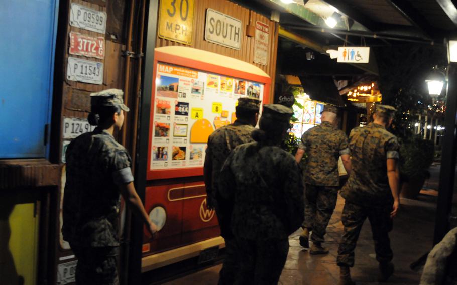 Five Marines in uniform walk in the evening on a street outside a bar.