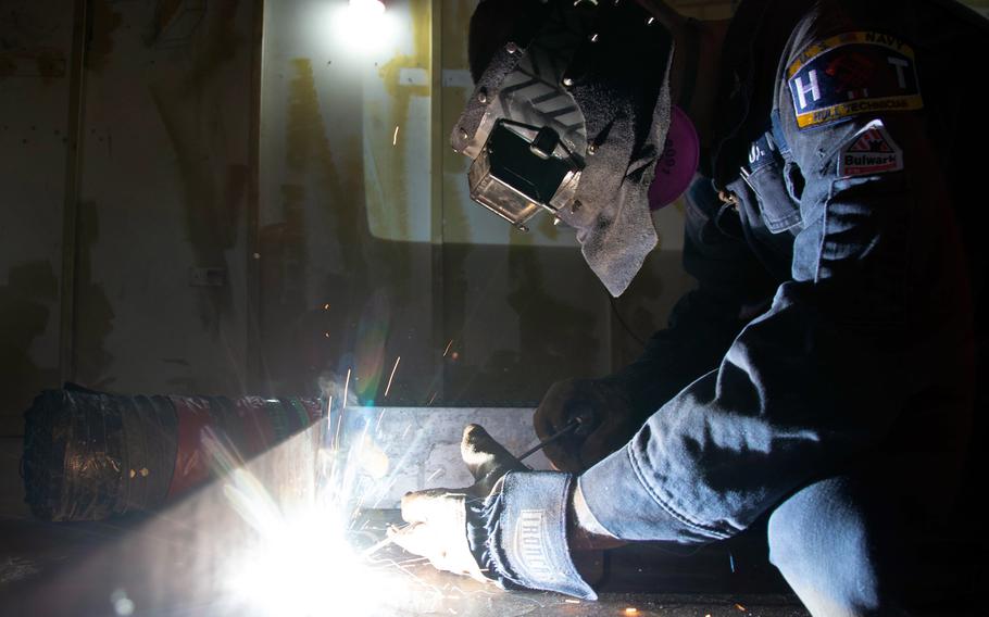 A sailor welds metal to the deck of an aircraft carrier.