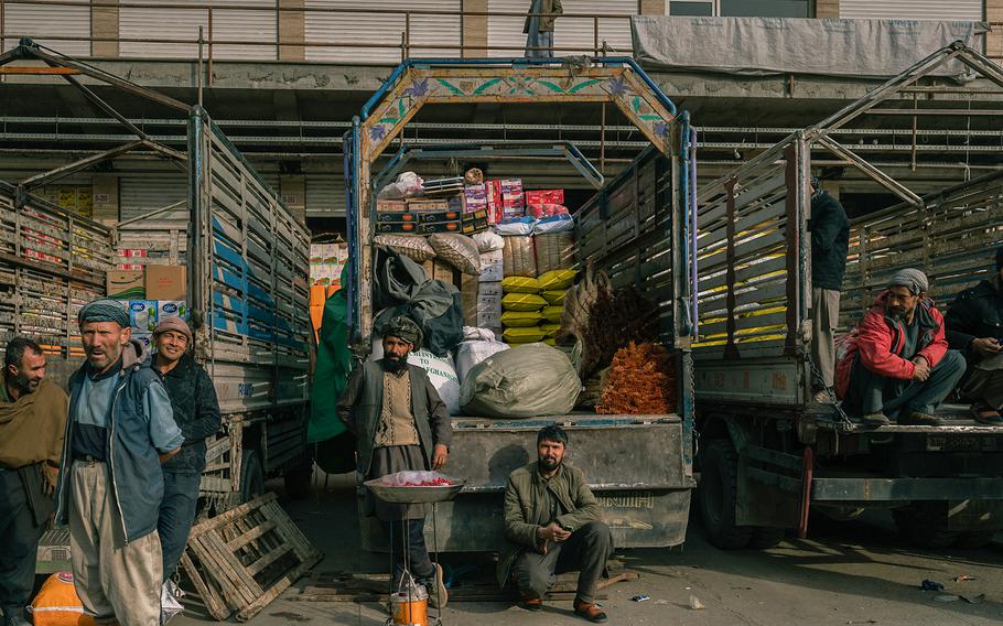 Men sit on their trucks after unloading products, while another sells pomegranate seeds, at Kabul’s main grain market.