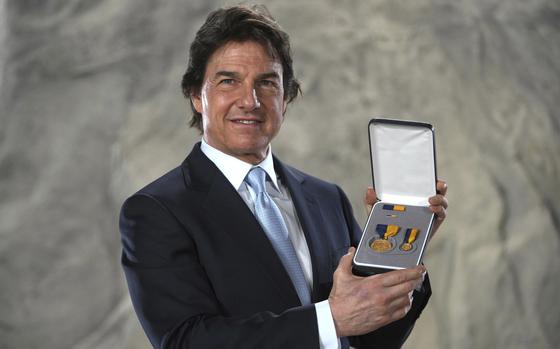 Tom Cruise poses in a suit while holding a case containing a Navy medal.