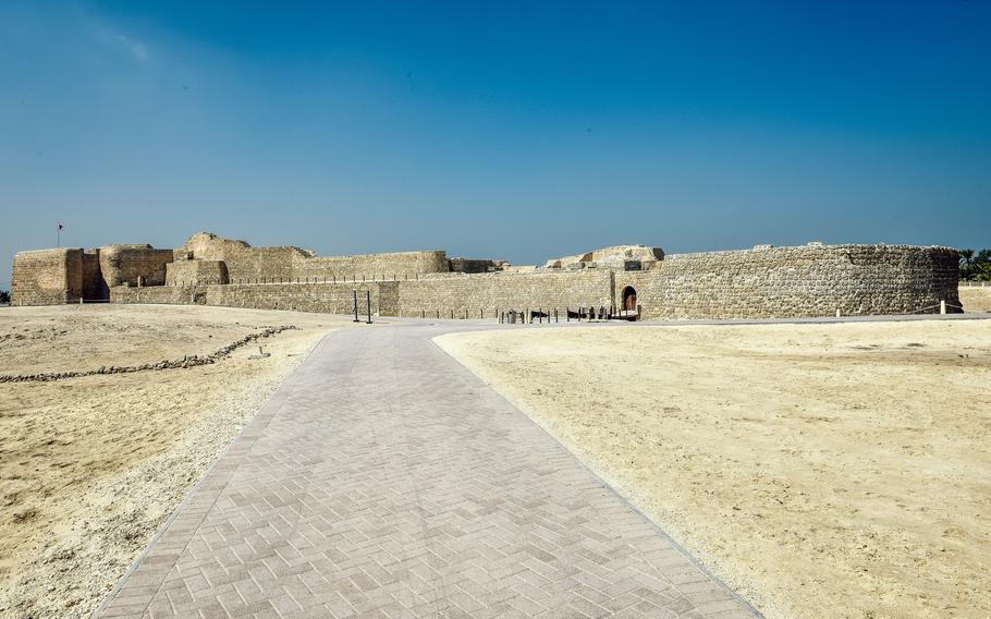 A long walkway leading to Qal’at al-Bahrain, or Fort of Bahrain, stretches about 300 meters from the gated entrance. The path curves around the entire ancient fort, showcasing its historic architecture.