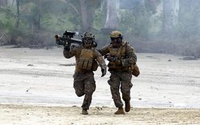 Two U.S. Marines in uniform run in the sand, with one carrying a missile launcher.